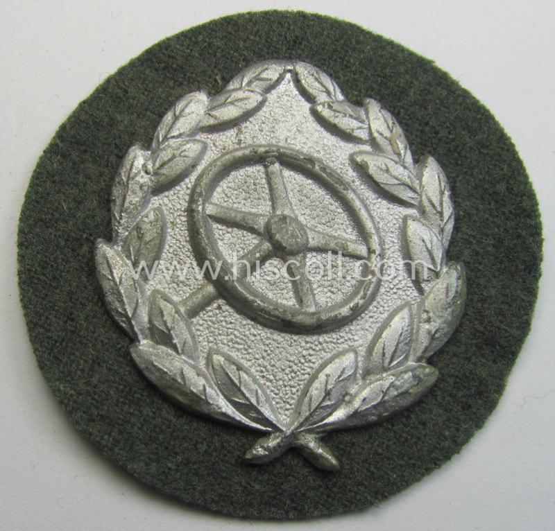 WH (Heeres- ie. Waffen-SS) so-called: 'Kraftfahrbewährungs-Abzeichen in Silber' (or: silver-class drivers' proficiency-badge) that comes mounted onto its piece of field-grey-coloured wool and that comes as probably issued- but never worn, condition