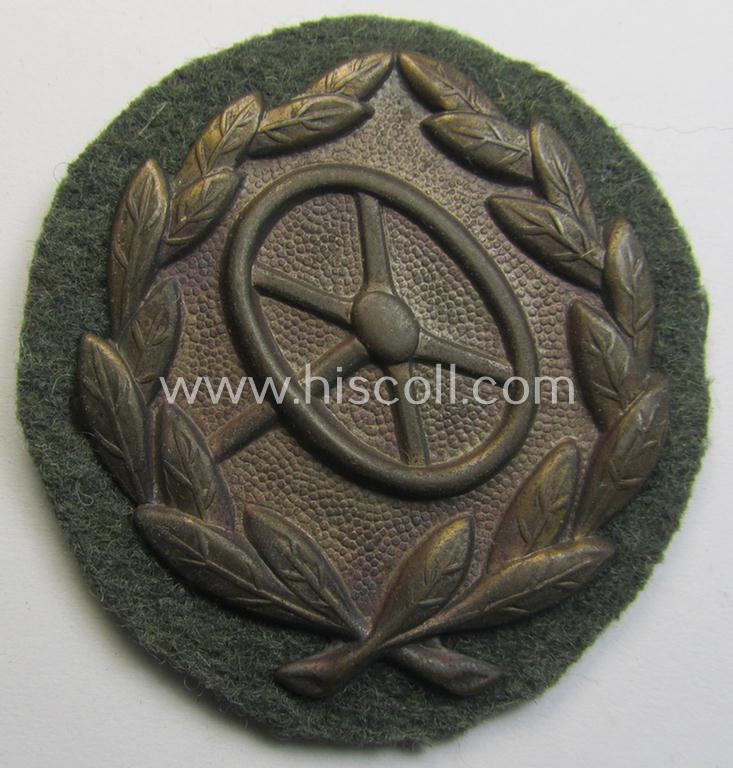 WH (Heeres- ie. Waffen-SS) so-called: 'Kraftfahrbewährungs-Abzeichen in Bronze' (or: bronze-class drivers' proficiency-badge) that comes mounted onto its piece of field-grey-coloured wool and that comes as probably issued- but never worn, condition
