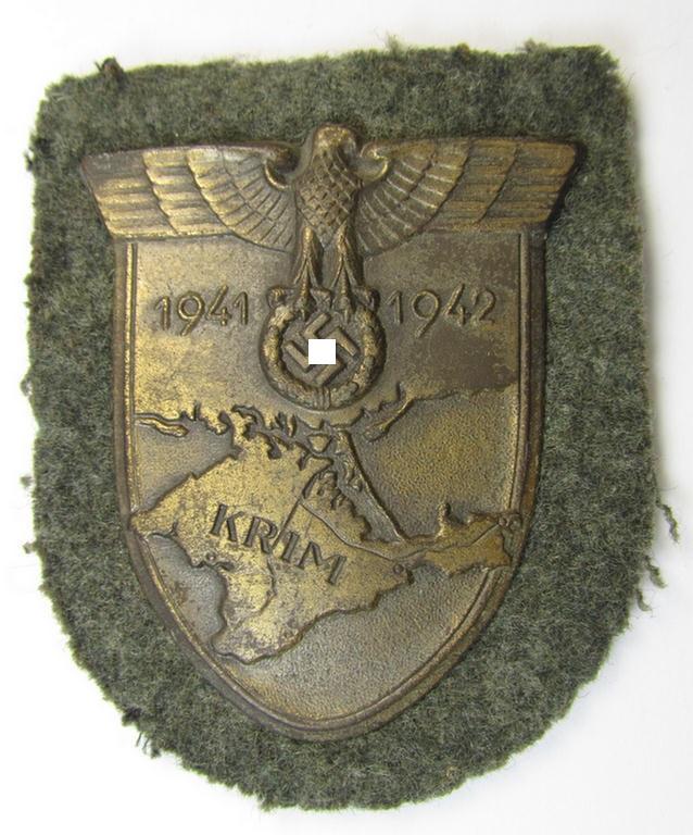 Attractive, WH (Heeres o. Waffen-SS) 'Krim'-campaign-shield that comes mounted onto its original, field-grey-coloured 'backing' and that comes in an issued-, minimally worn and/or carefully tunic-removed-, condition