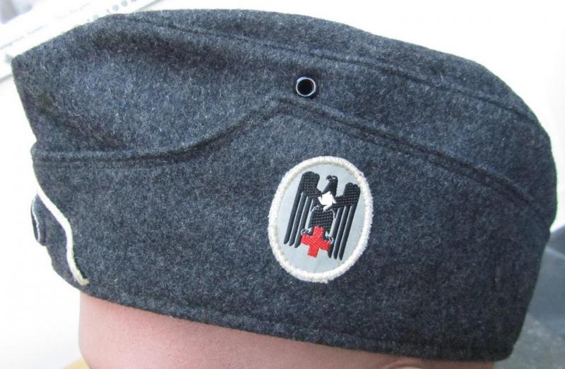 Attractive, typical darker-greyish-blue-coloured, so-called: German Red Cross (ie. 'Deutsches Rotes Kreuz' or: 'DRK' EM- (ie. NCO-) type side-cap (ie. 'Schiffchenmütze für Mannschaften u. Unteroffiziere des deutschen Rotes Kreuzes')