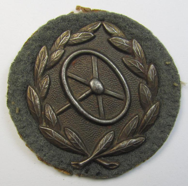 WH (Heeres- ie. Waffen-SS) so-called: 'Kraftfahrbewährungs-Abzeichen in Bronze' (or: drivers' proficiency-badge in bronze) that comes mounted onto its piece of field-grey-coloured wool as most certainly issued- and moderately worn, condition