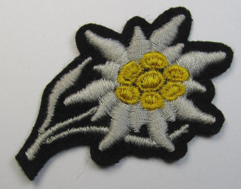Waffen-SS-pattern, black-coloured M43-cap-insignia (ie. 'Mützenabzeichen') depicting an: 'Edelweiss'-flower as was specifically used by the various 'Gebirgsjäger'- (ie. mountain-troops-) related divisional-staff