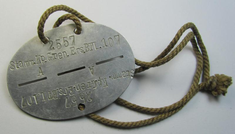 Attractive, aluminium-based, WH (Heeres) related ID-disc bearing the clearly stamped unit-designation that reads: 'Stamm.Kp.Gren.Ers.Btl.107' and that comes still mounted onto its (period-attached) cord as issued- and/or worn