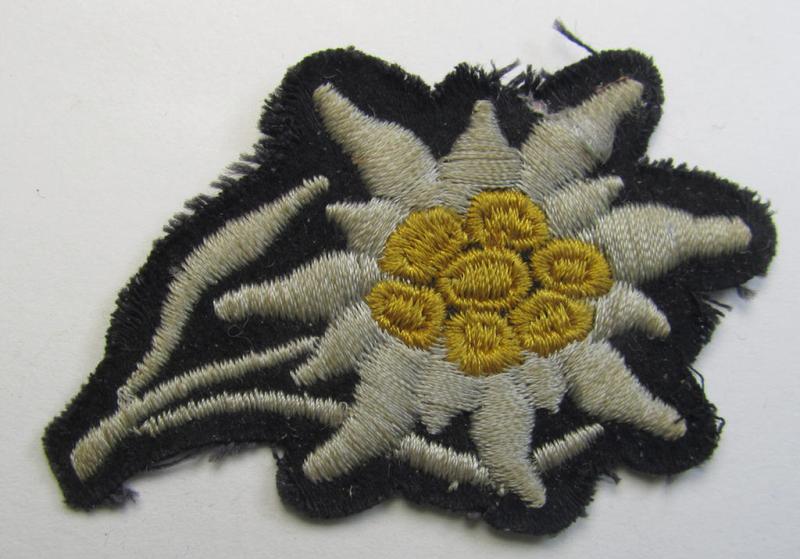 Truly used, Waffen-SS-pattern black-coloured M43-cap-insignia (ie. 'Mützenabzeichen') depicting an: 'Edelweiss'-flower as was specifically used by the various 'Gebirgsjäger'- (ie. mountain-troops-) related divisional-staff