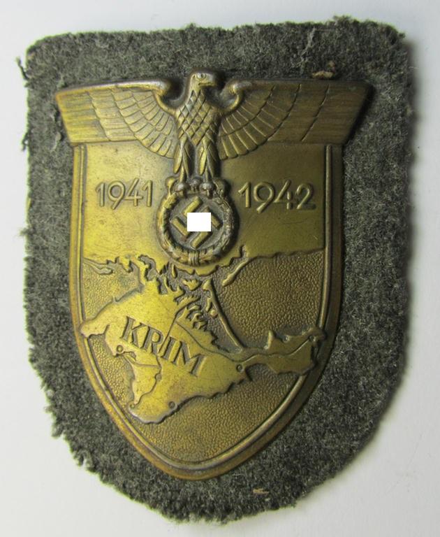 Attractive, WH (Heeres o. Waffen-SS) 'Krim'-campaign-shield (by the 'Wilh. Deumer'-company) that comes mounted onto its original, field-grey-coloured 'backing' and that comes in an issued-, moderately worn and/or carefully tunic-removed-, condition