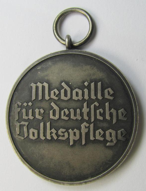 Attractive, silver-toned (and I deem 'Buntmetall'-based!) 'Deutsche Volkspflege'- (ie. civil-service) medal being a non-maker-marked example that came together with its (confectioned- and somewhat shortened) ribbon (ie. 'Bandabschnitt')
