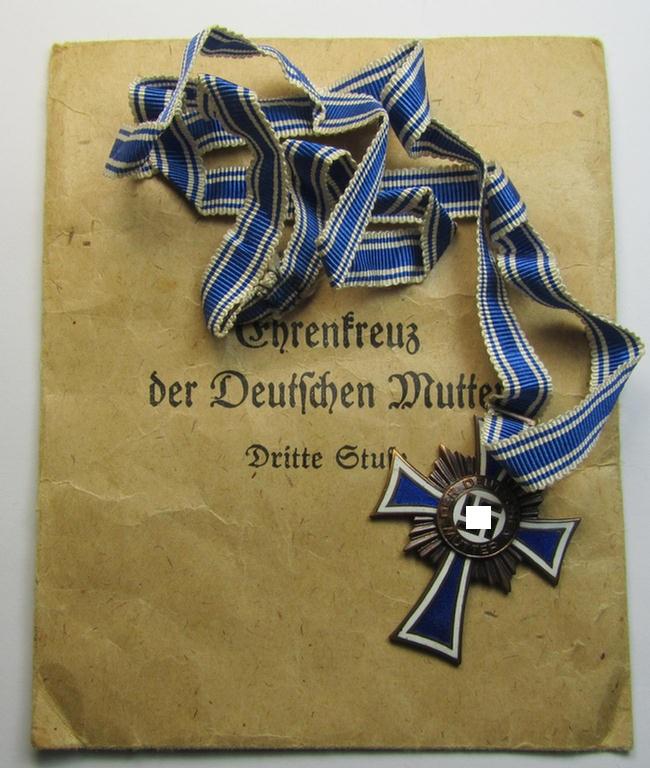 Attractive, 'Ehrenkreuz der deutschen Mutter - dritte Stufe' (or: bronze-class mothers'-cross) that came mounted onto its long-sized ribbon and that came stored in its period pouch (by the maker: 'Jakob Bengel - Idar-Oberstein')