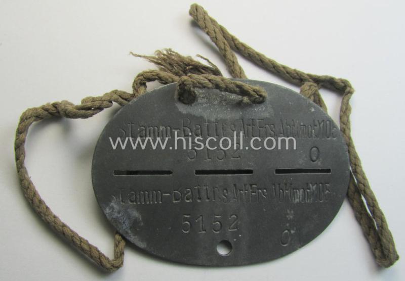 Zinc-based, WH (Heeres) ie. 'schwere Artillerie'-related ID-disc bearing the clearly stamped unit-designation: 'Stamm-Battr.s.Art.Ers.Abt.(mot) 105' and that comes mounted onto its period cord as issued and worn