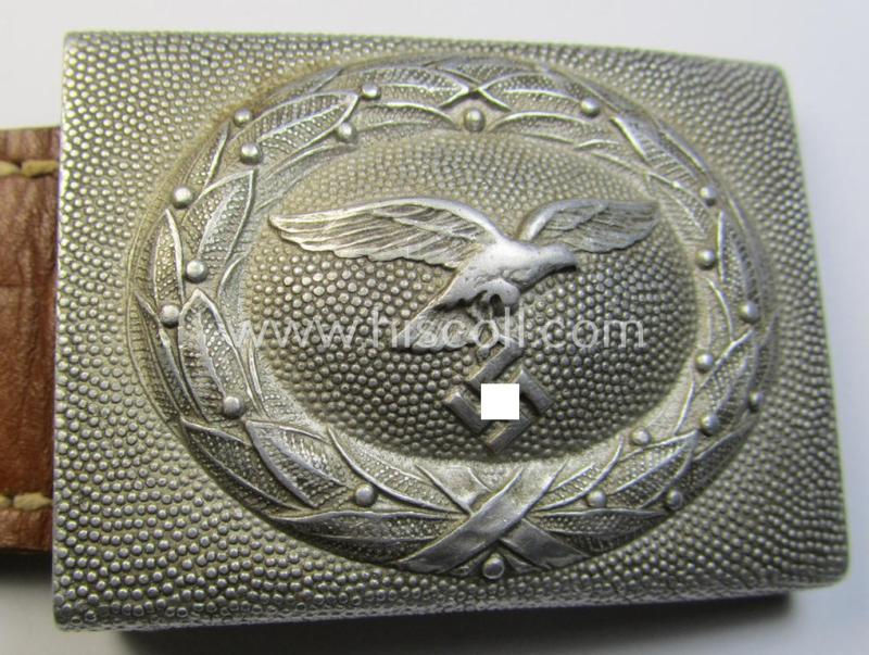 Attractive, WH (Luftwaffe) silver-coloured and aluminium-based belt-buckle, being a maker- (ie. 'F.W. Assmann & Söhne'-) marked example that comes mounted onto its leather-based tab and that comes in a minimally used condition