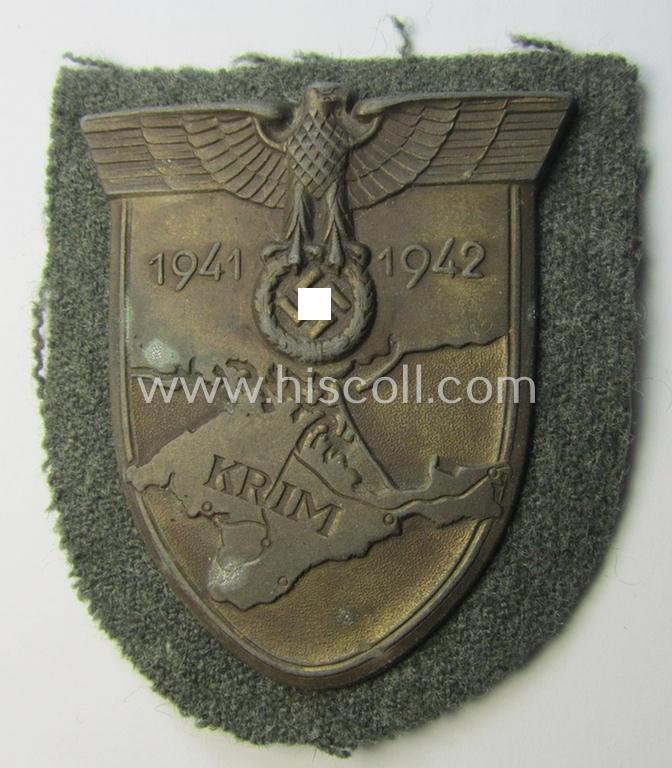 Attractive, WH (Heeres o. Waffen-SS) 'Krim'-campaign-shield that comes mounted onto its original, field-grey-coloured 'backing' and that comes in a surely issued-, minimally worn and/or (I deem) carefully tunic-removed-, condition