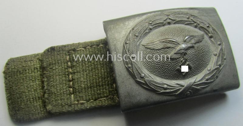 WH (Luftwaffe) 'tropical-issued' belt-buckle being a non-maker-marked, greyish-silvercoloured example that comes mounted onto its original, greenish-coloured- (and/or: 'webbing'-based-) tab
